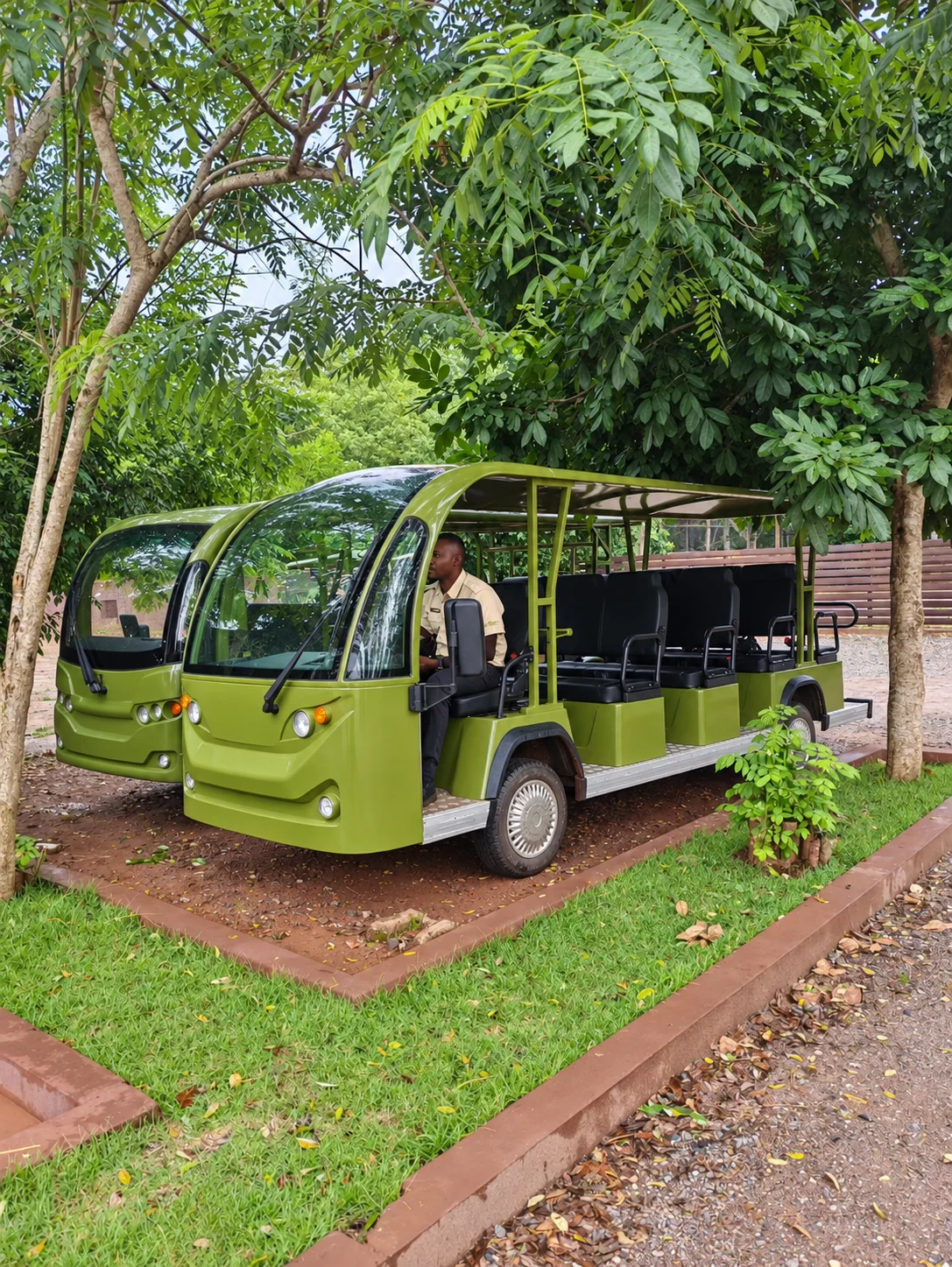 Two green passenger shuttles on a tree-lined path